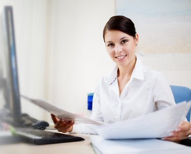 Eine Frau sitzt vor einem Computer und ordnet Papiere.