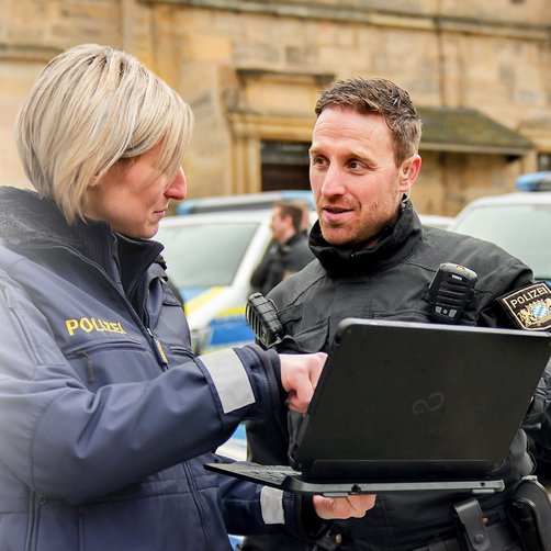 Eine Frau und ein Mann in Polizeiuniform unterhalten sich, während die Frau einen Laptop hält.