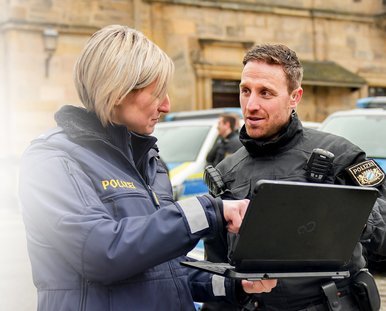 Eine Frau und ein Mann in Polizeiuniform unterhalten sich, während die Frau einen Laptop in der Hand hält.