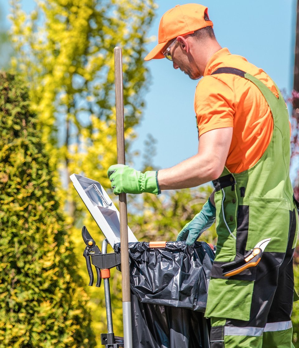 Ein Mann in Arbeitskleidung kümmert sich um den Abfall im Garten.