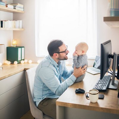 Ein Mann hält ein Baby im Arm, während er an einem Schreibtisch sitzt.