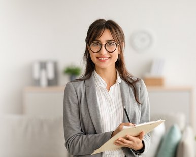 Eine lachende Frau in Business-Kleidung schreibt etwas auf einen Zettel.