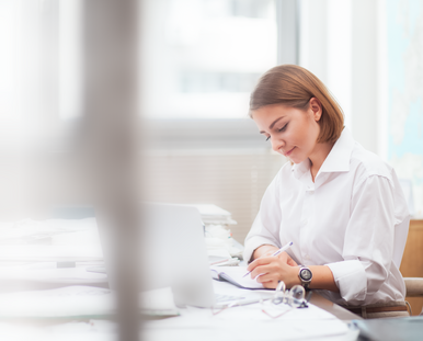 Eine Frau in weißer Bluse arbeitet an ihrem Laptop