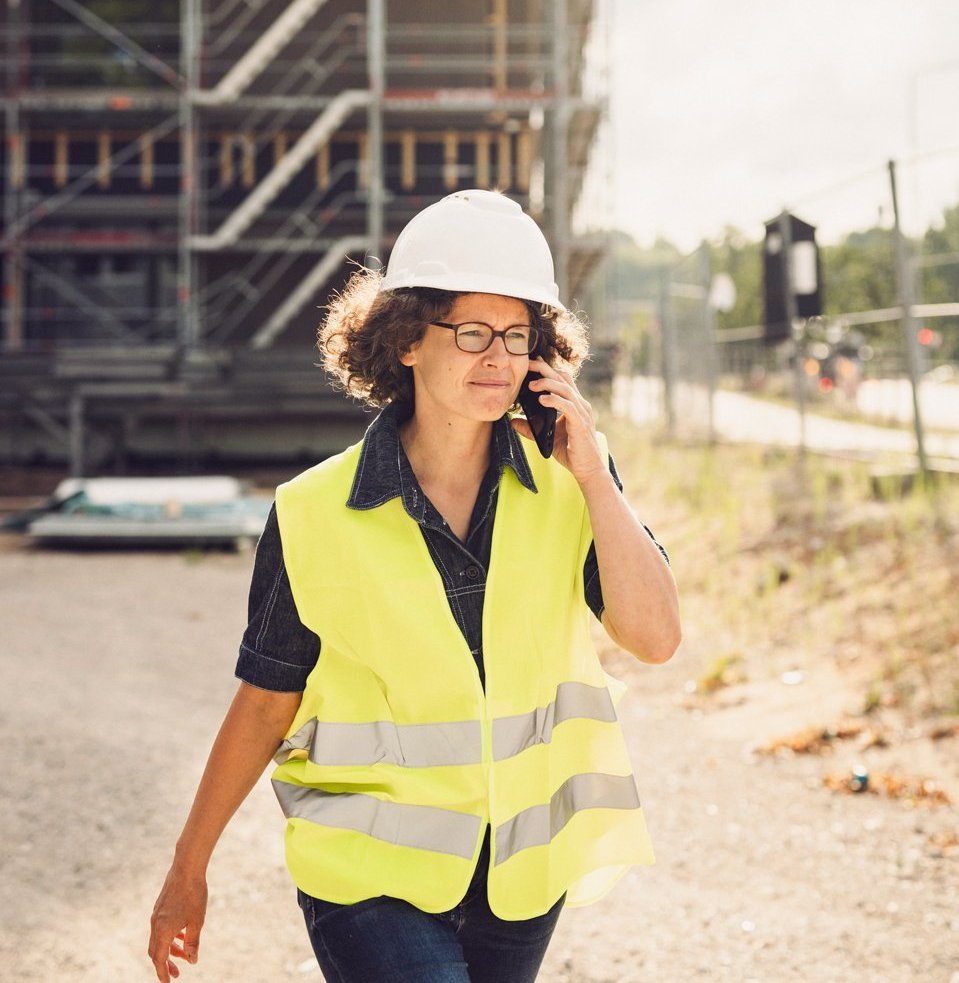 Eine Frau in Sicherheitskleidung läuft über eine Baustelle und telefoniert.