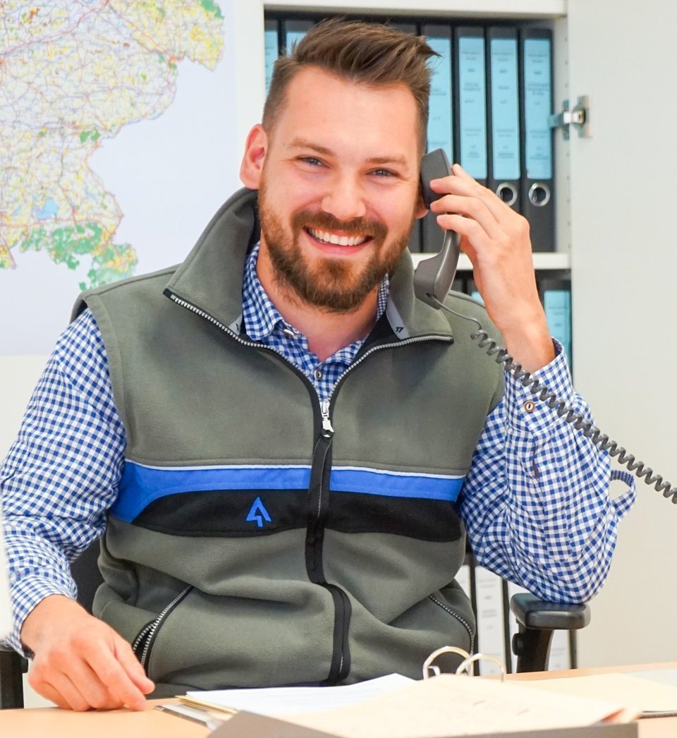 Ein lachender Mann sitzt am Schreibtisch und telefoniert.