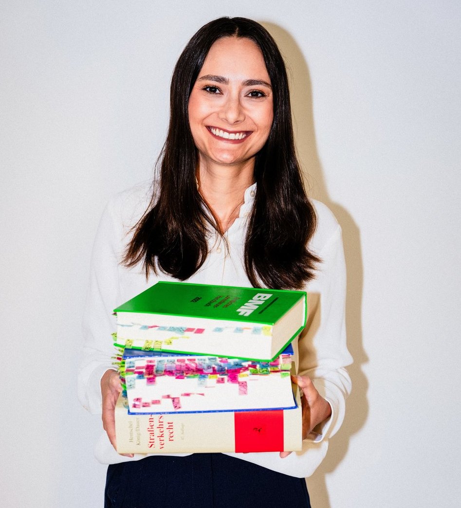 Junge Frau mit schwarzen Haaren hält drei Gesetzesbücher in den Händen.