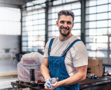 Ein lachender Mann in einer Werkstatt trägt einen Blaumann.