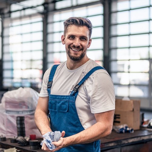 Ein lachender Mann in einer Werkstatt in einem Blaumann.