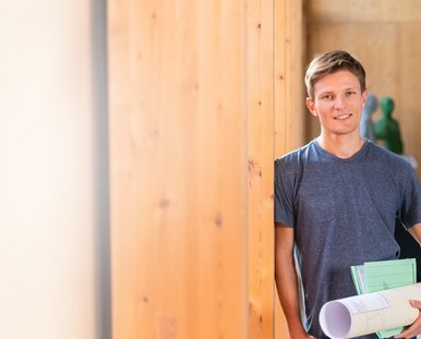 Mann mit Papierrolle lehnt an Holzwand 