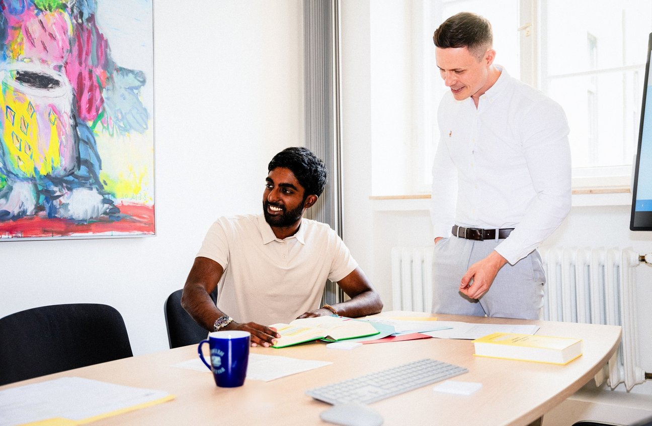 Zwei Männer besprechen Unterlagen an einem Besprechungstisch in einem hellen Büro.