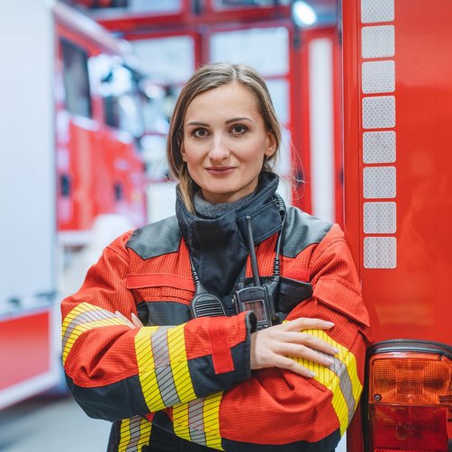 Eine lächelde Frau in Feuerwehruniform an einem Feuerwehrwagen.