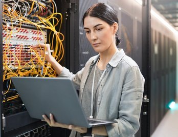 Eine Frau arbeitet an einem Laptop in einem Serverraum.