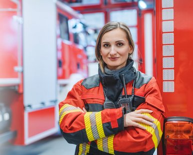 Eine lächelde Frau in Feuerwehruniform an einem Feuerwehrwagen.