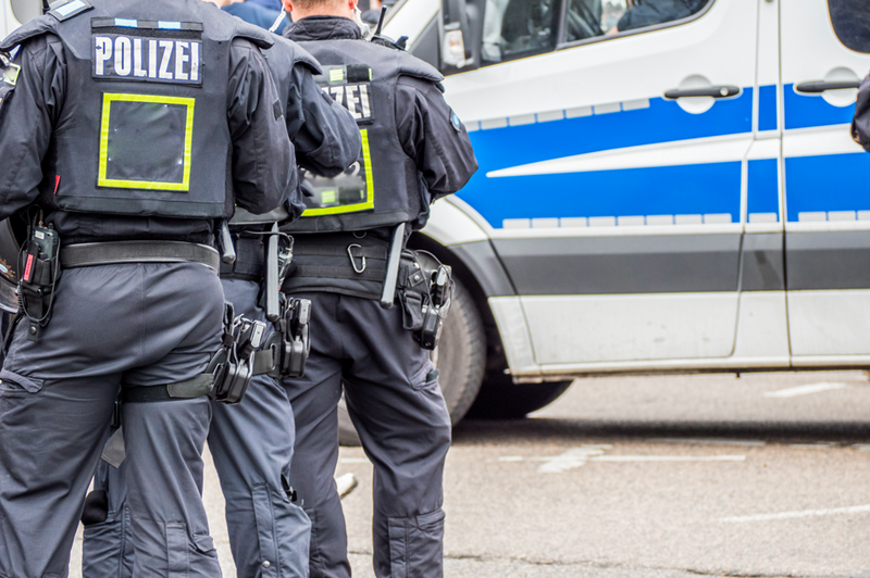 drei Personen in Polizeisicherheitsuniform stehen vor einem Polizeiwagen.