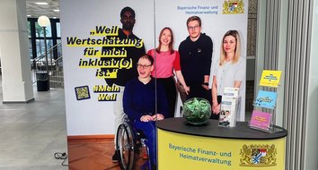 Das Bild zeigt einen Messestand mit Messewand und einem Tresen. Auf der Messewand ist ein Bild mehrerer Personen zu sehen, u. a. eine Person im Rollstuhl. Zudem ist der Spruch aufgedruckt: "Weil Wertschätzung für mich inklusiv(e) ist."