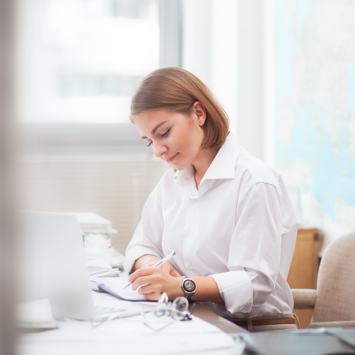 Eine Frau in einer weißen Bluse arbeitet an ihrem Laptop.