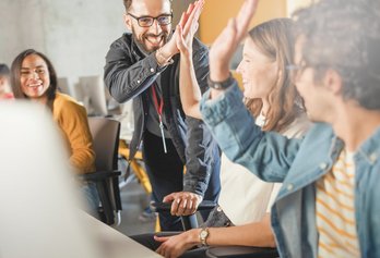 Eine Gruppe von Personen im Büro, während ein Mann einen High Five gibt.