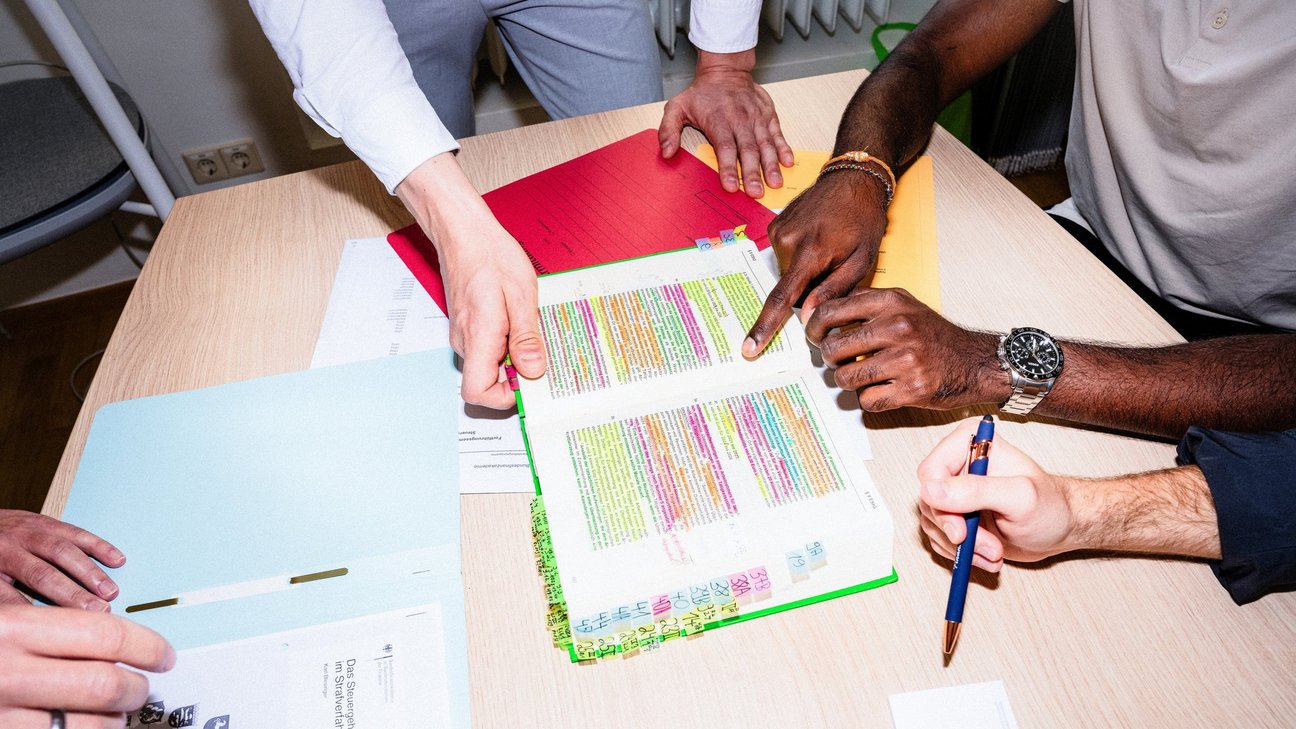 Mehrere Personen sitzen an einem Tisch und besprechen gemeinsam das farbig markierte Einkommensteuerhandbuch.