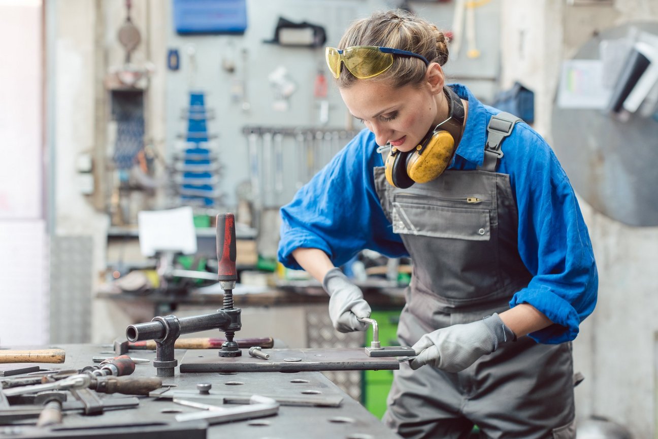 Eine Frau in Arbeitskleidung arbeitet mit Metallen.