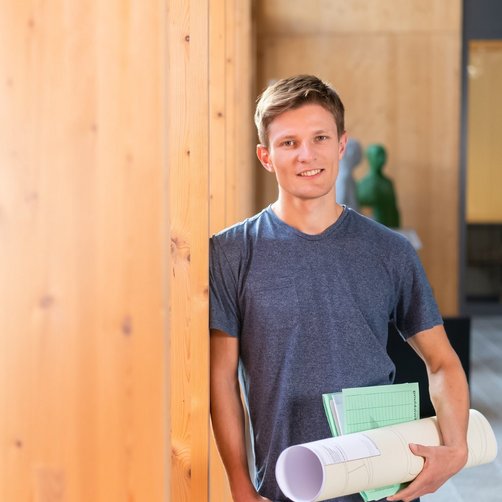 Mann mit Papierrolle lehnt sich an Holzwand