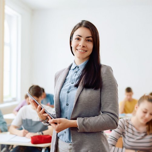 Eine Frau steht vor einer Klasse und hält ein Tablet in der Hand.