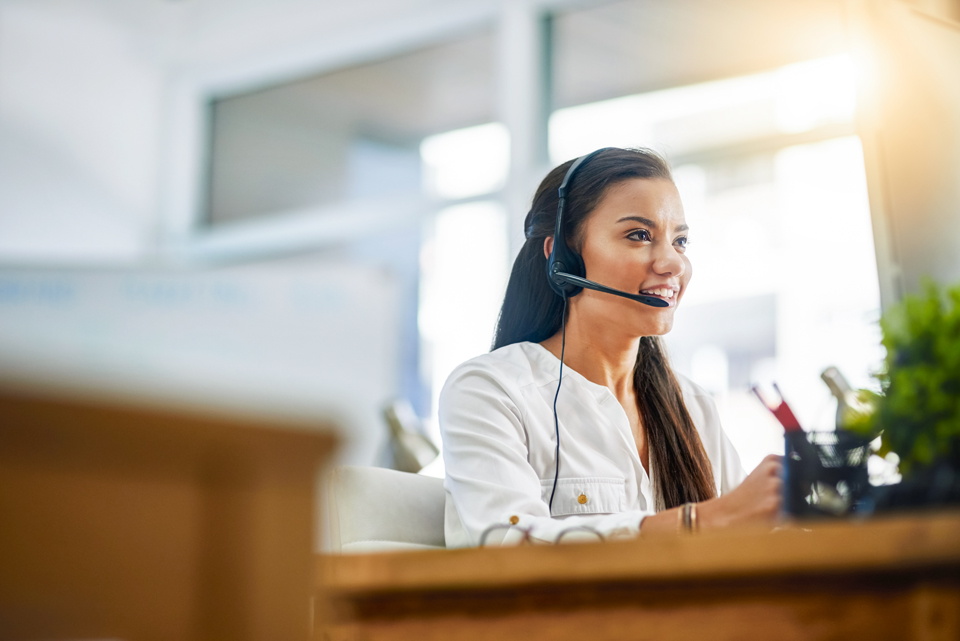 Eine lachende Frau mit Headset auf dem Kopf telefoniert.