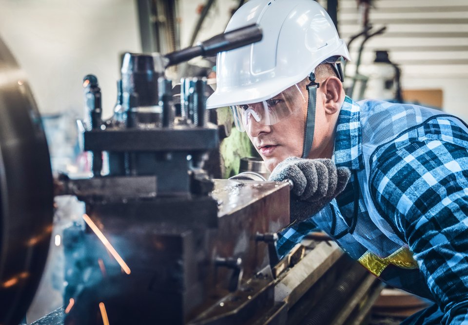 Ein Mann arbeitet an einer Maschine mit Sicherheitshelm