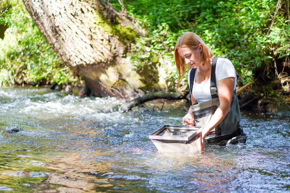 Eine Frau in einem Fluss, welche das Wasser siebt.