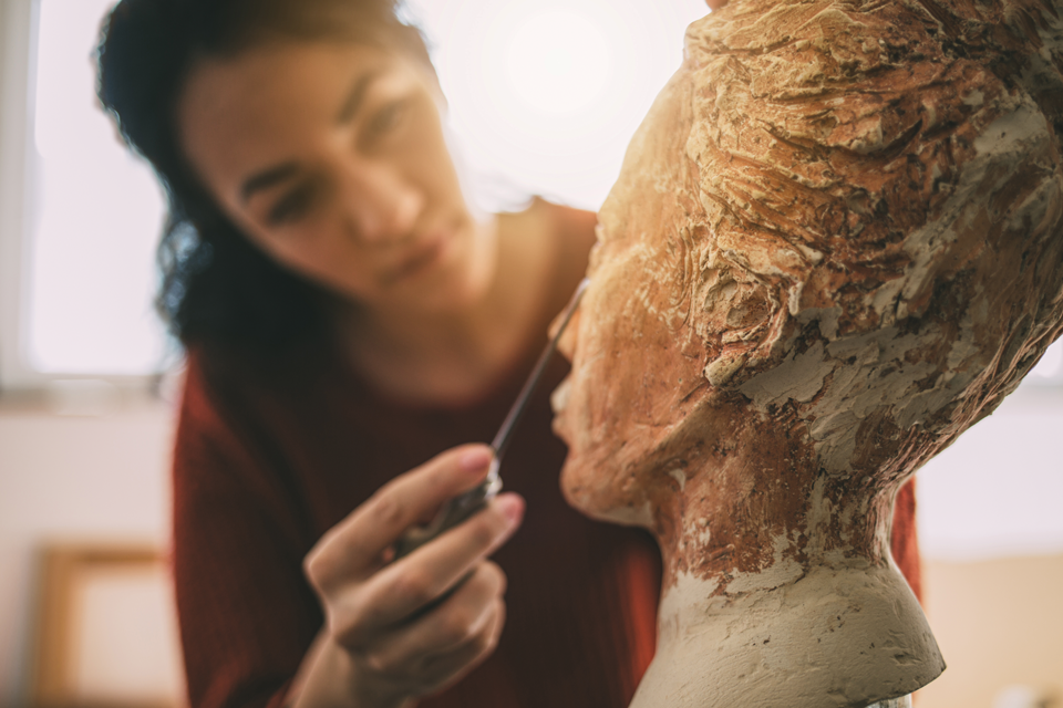 Eine Frau schnitzt an einer Steinskulptur.