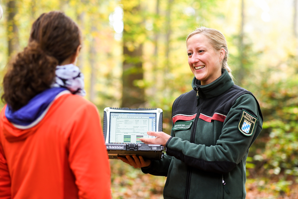 Zwei Frauen stehen im Wald und schauen sich etwas auf dem Tablet an.