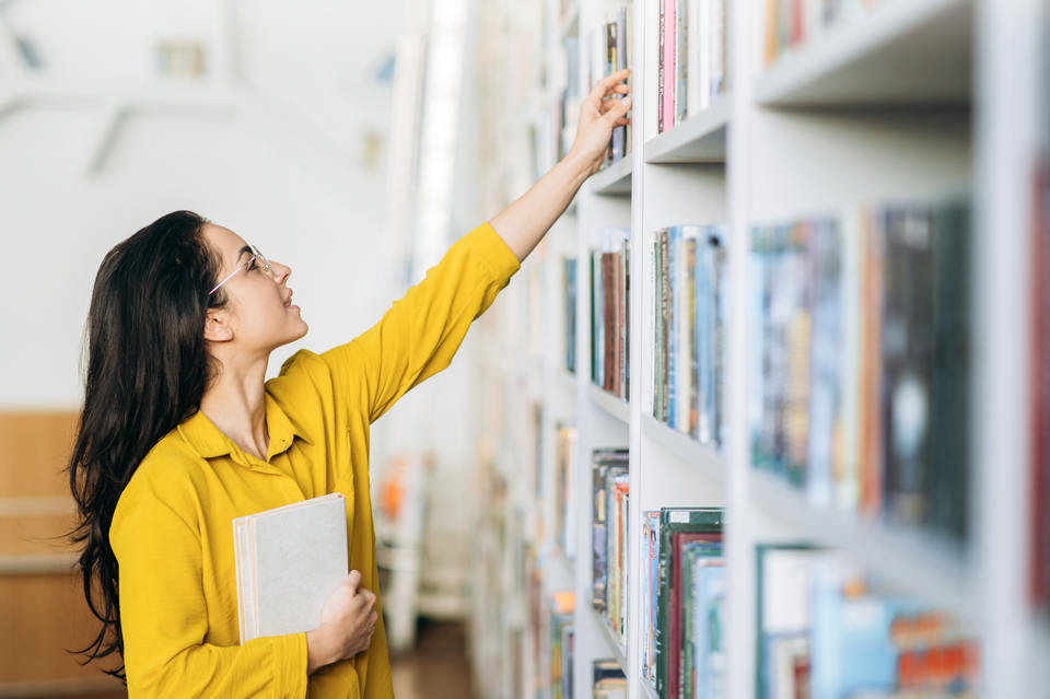 Eine Frau stöbert in einem Bücherregal und greift nach einem Buch.