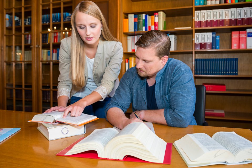 Eine Frau und ein Mann sitzen an einem Tisch und durchstöbern verschiedene Bücher.