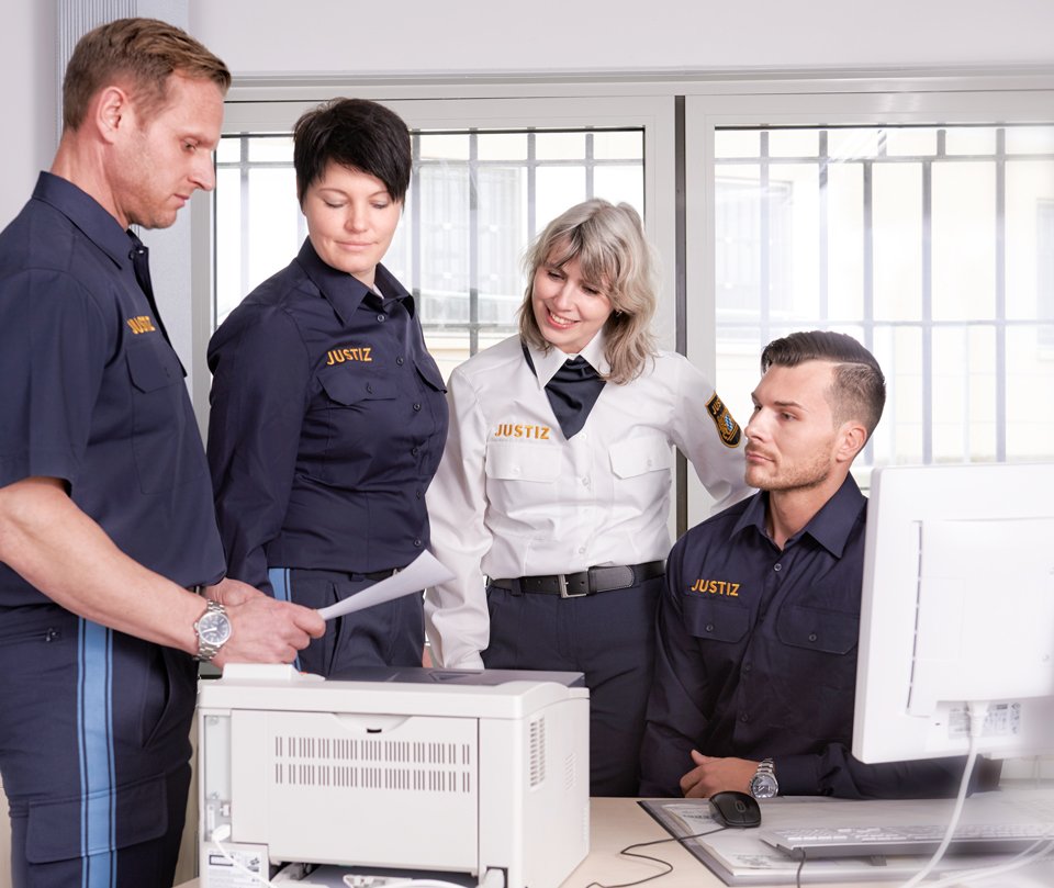 Vier Personen in einem Büro, gekleidet in Justizuniform, schauen auf einen Zettel.